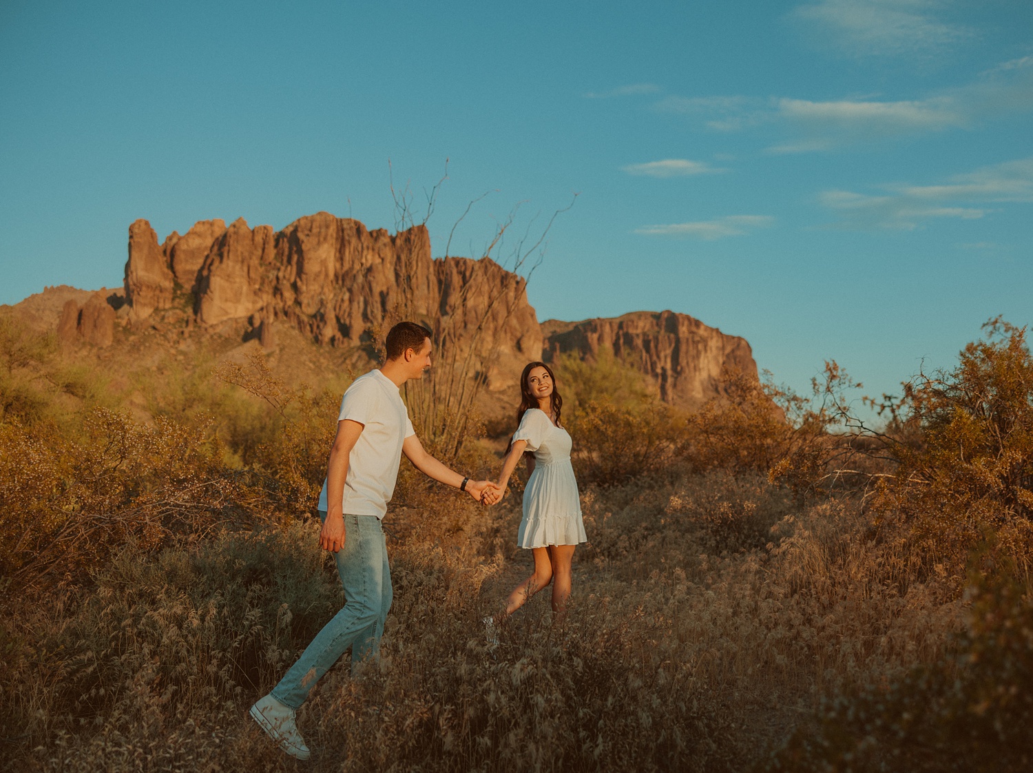 a couple walking in front of superstition mountains at lost dutchman state park during their engagement photos