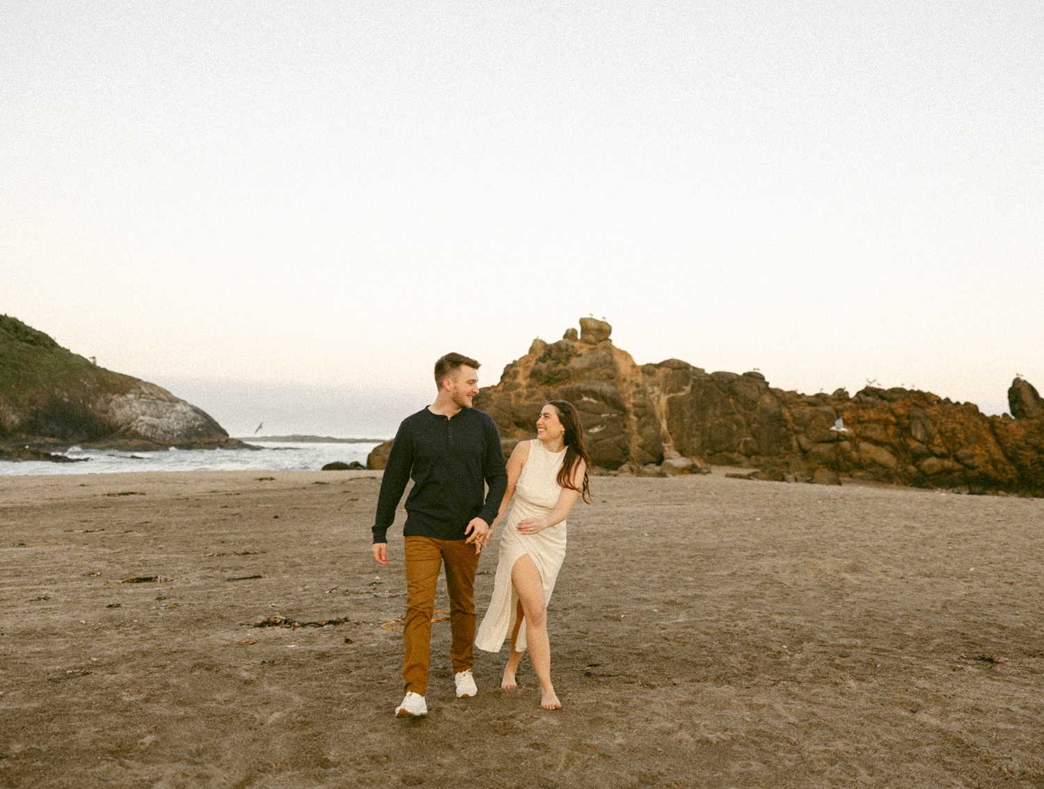 a couple walking along North Fogarty Beach together at sunrise for engagement photod